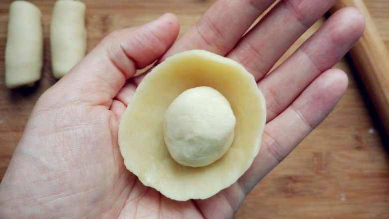 豆沙蛋黄酥, 取一块水油皮，两手大拇指在内，其余手指在外，边捏边转动，形成一个中间凹的圆饼，把油酥团成球，放在中间