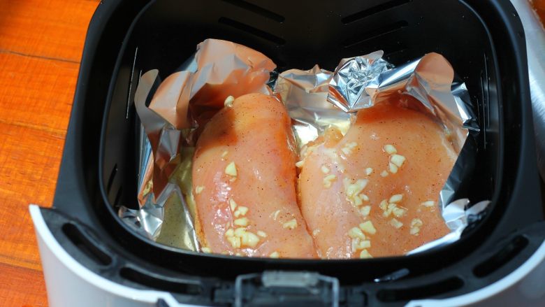 香蒜蜂蜜烤鸡胸,空气炸锅的炸篮里铺一张锡纸，把腌制好的鸡胸肉放到里面。