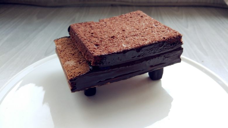 可可钢琴蛋糕,将钢琴支架顶部粘少许黑巧克力，放在盘中合适位置，将钢琴主体放在上面，侧面涂少许巧克力（或甘纳许）