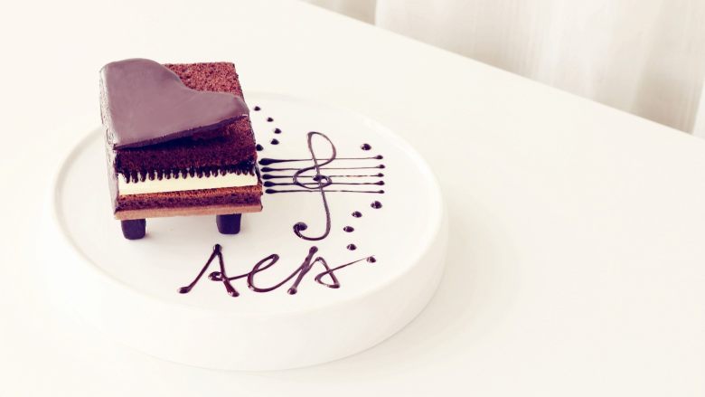 可可钢琴蛋糕,将凝固的钢琴盖放在顶部，一侧用一小块蛋糕体支撑起，另用黑巧克力在盘上画出音符即可