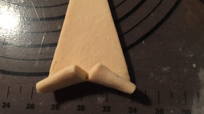 流沙起酥包,取一个小三角形面片，在三角形底部中点处划一道口子；用两只手，捏住两个角，向上卷在顶部的小尖上刷一层全蛋液