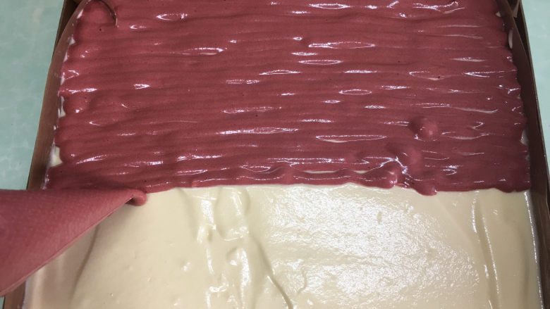红丝绒旋风蛋糕卷,将裱花袋中的红曲粉蛋糕液均匀的挤在原味蛋糕糊上。