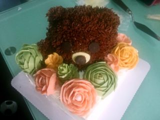 立体小熊蛋糕,用黑白巧克力做出眼睛、嘴巴、耳朵，把裱花的花摆上