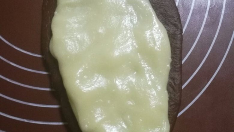 可可麻薯软欧包,将一个可可面团用擀面杖擀成牛舌片状，戴上一次性手套把一份麻薯拉成比牛舌状小一圈的面片，放在可可面片上