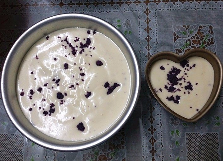 紫薯裱花酸奶蛋糕,倒入模具中再轻震几下，震出大气泡后表面再撒入少许紫薯碎