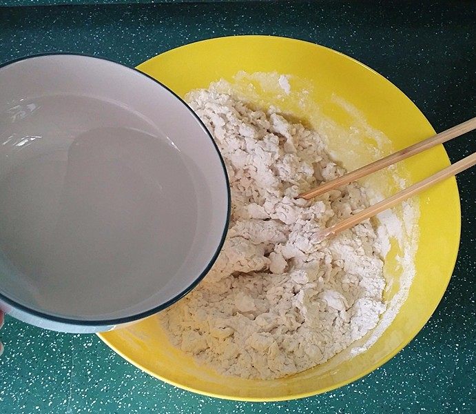 豆腐锅巴韭菜盒子,将热水一边倒入面粉，一边搅拌成絮絮状