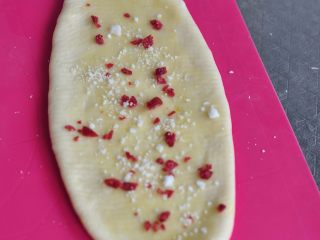 千层蔓越莓土司,取一个小面团，从中间压上，擀了上半部分再擀下半部分，擀成椭圆形，表面刷一层软化的黄油，撒上切碎的蔓越莓颗粒和椰蓉。然后再这样操作剩下的面团，
