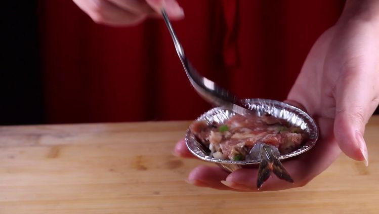往虾里打入一颗蛋——虾扯蛋,然后借用勺子的底部，将肉馅压平。用勺子在肉馅上挖一个小的凹槽。