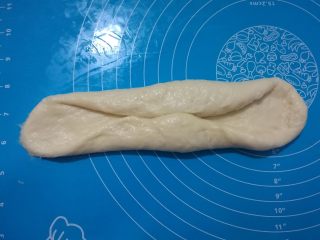 一次发酵软吐司,取出其中一个面团，擀成长舌状。两边往中间对折，稍微压扁。