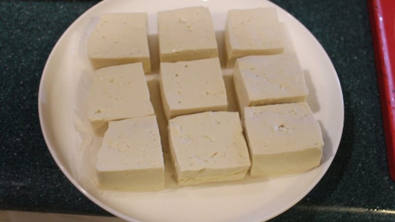  青酱烤豆腐,木棉豆腐水分很多，先要压去部分水分。将纸巾或毛巾垫在盘子下，平放上豆腐。