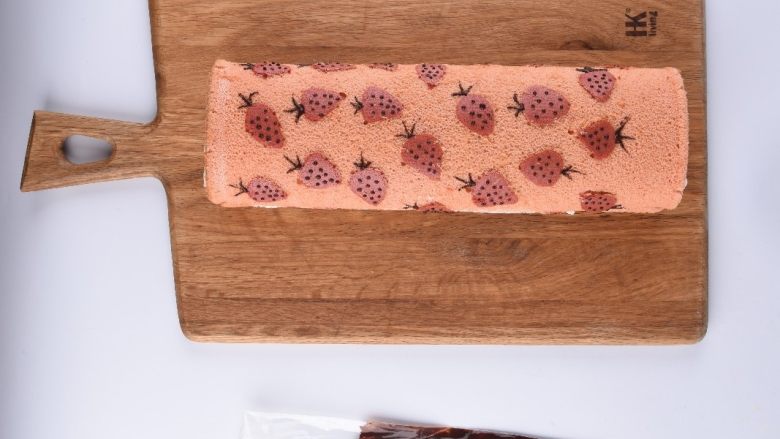 草莓花式蛋糕卷,可可糊装入裱花袋里，在蛋糕卷草莓部分点上小点，画出叶子