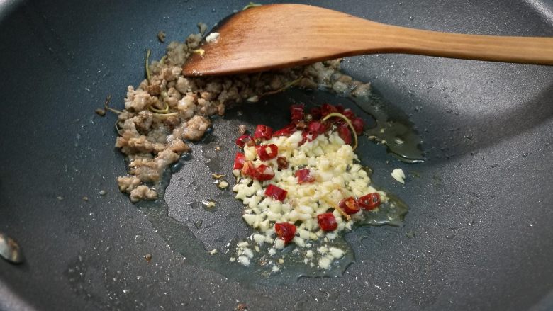 腌酸豆角懒人法,将肉末划到锅一边，放入蒜末，辣椒在油里煸香。