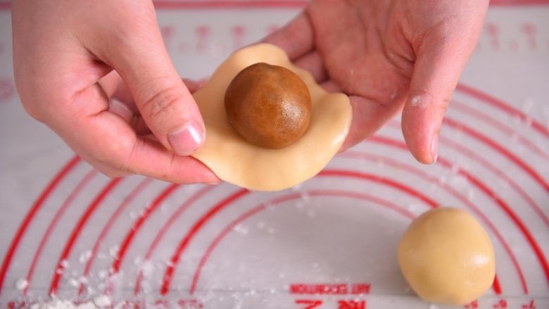 【烘焙配方】经典广式月饼,硅胶垫上撒少量粉，取一个小面团用手压扁，中间放一颗月饼馅