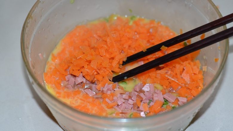胡萝卜火腿煎蛋，越吃越爱,切好的火腿粒，韭菜粒，焯过水的胡萝卜粒都放在碗中，跟蛋液拌在一起。
