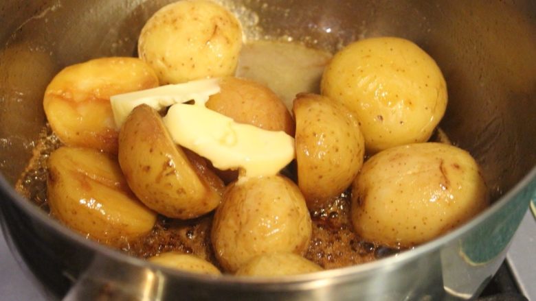 土豆甘露煮,其实这时已经完成甘露煮。不过今天来多道步骤让味道更丰富。放入奶油，摇动锅子，让融解的奶油均匀裹上每个土豆。