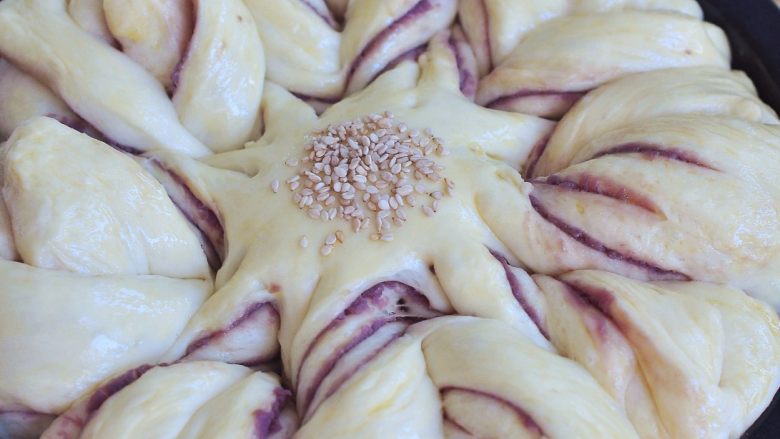 花朵紫薯面包,面团发酵至满模后，表面刷一层蛋液，中间处撒上<a style='color:red;display:inline-block;' href='/shicai/ 678'>白芝麻</a>。放入烤箱中，170度烘烤20分钟。
