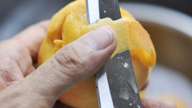 自制黄桃罐头,用水果刀削掉黄桃的外皮，把黄桃切开挖出桃核。