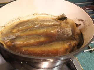 香鱼甘露煮,中间偶而摇动一下锅子，让煮汁能淋在鱼身上，使之均匀入味。