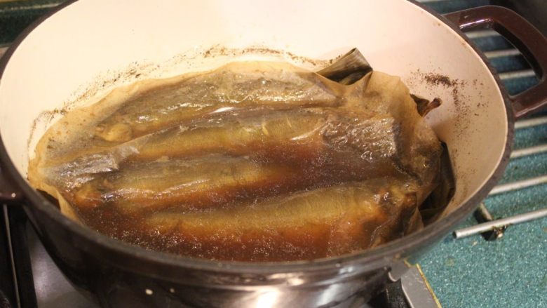 香鱼甘露煮,中间偶而摇动一下锅子，让煮汁能淋在鱼身上，使之均匀入味。