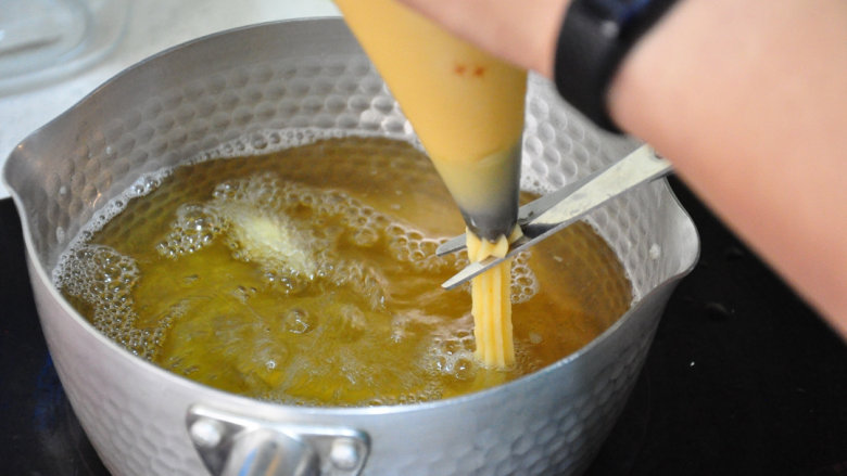 西班牙油条——吉拿果,从裱花袋挤出约10cm长的面糊，再用剪刀剪断，让面糊掉入油锅中。