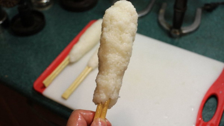 烤米卷,将饭团沿竹筷捏成长条型。