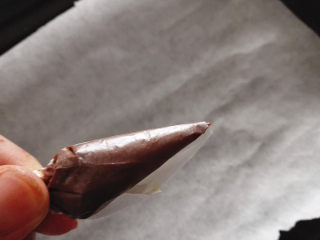 万圣节之黑芝麻球——蜘蛛&小精灵,油纸折成一个三角形的小包，把软化好的巧克力放在里面，前端剪开一个小口