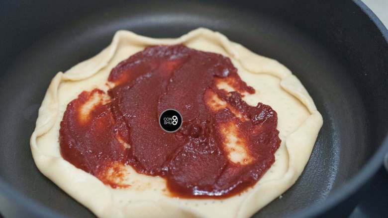 没有烤箱照样做出香浓芝士风味薄底披萨,锅底抹一层油，放入饼皮。抹上厚厚的番茄酱。