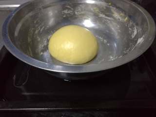面包入门基本功之黄油面包卷,用两手轻轻将面团扒至近处，使面团表面鼓胀起来。然后面团放在面盆里，盆放在加了热水的烤盘里。
