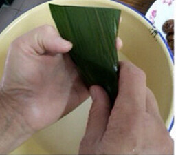 蜜枣花生粽,将粽叶的尾部折过盖起来，左手托好粽子，右手把粽叶尾部对折