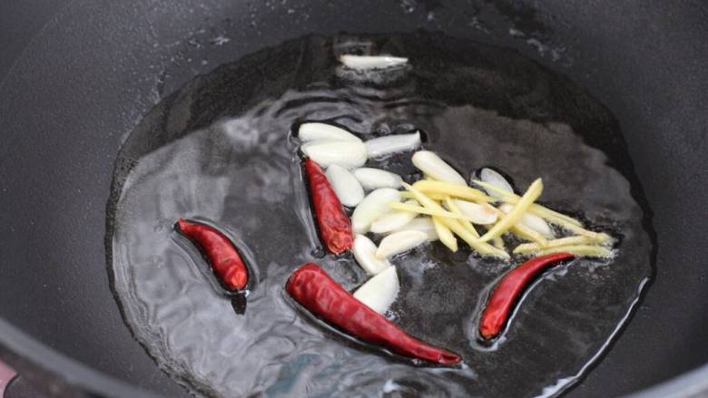 芹菜炒墨鱼,锅中倒适量食用油烧热，下姜丝、蒜片和红干椒小火炒出香味儿。