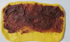 南瓜豆沙辫子面包,取一份面团，擀开成长方形。 表面均匀涂抹上豆沙馅，尾部留出部分空隙