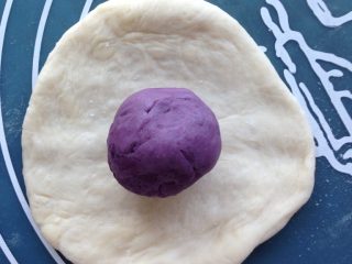 Q弹紫薯馅花朵面包,排好气后取出面团，分割成5等份，滚圆，放松10分钟。紫薯馅也分成5等份，搓圆。然后将小面团擀成圆形，翻面，包入紫薯馅。捏紧收口。