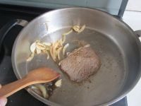 香煎牛扒,如图肉微微变色后再翻一面煎， 在锅的一边放入腌过洋葱和蒜片放在一边翻炒一下；