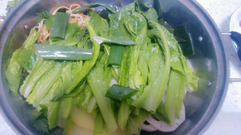 火锅鱼,上面铺上青叶菜和几根大葱叶和芹菜叶段。