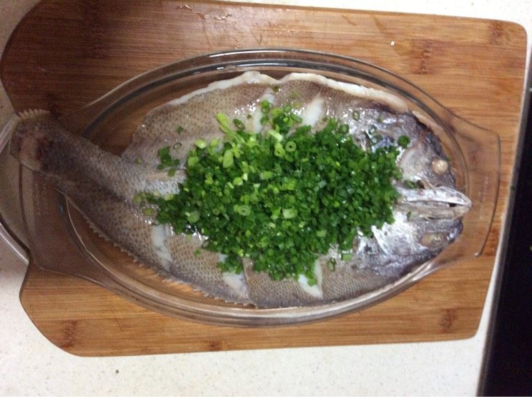 新手级别宴客菜 油葱鮸鱼,如图鱼出锅后倒去盘内蒸鱼后所留汤汁，并把底下葱白段抽出，铺上葱末