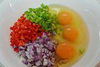 巴基斯坦炒蛋,将鸡蛋磕入碗中，放入红椒丁、青椒丁、洋葱丁