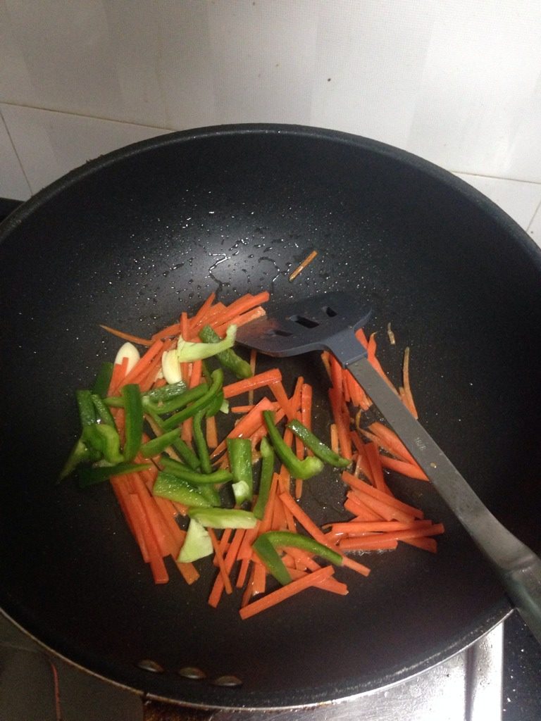 青椒萝卜炒豆干肉丝,如图洗锅重新起锅，放入蒜头、胡萝卜、青椒。炒至软身