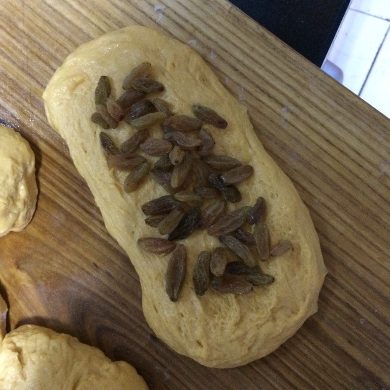 南瓜葡萄干面包,如图将面团压扁，放上葡萄干，从一段卷起，卷成卷