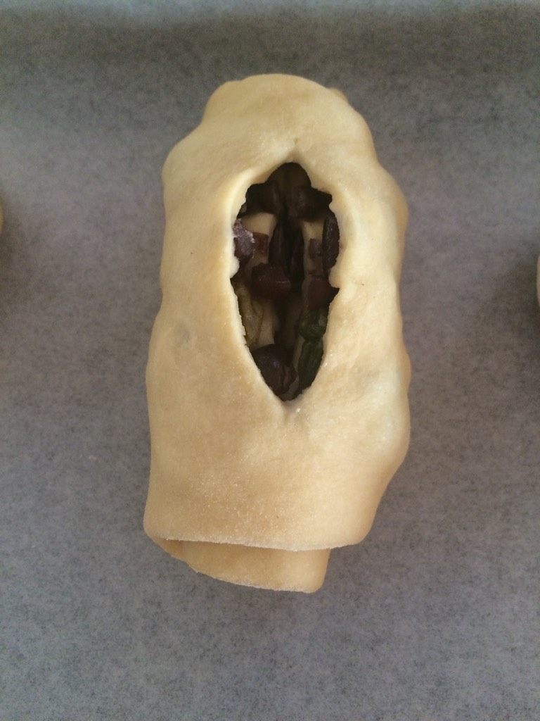 蜜豆面包,如图从一头卷起至尾部，收口朝下，中间用刀切出一个口子（不必太深），放在垫好油纸的烤盘上，依次全部做好；