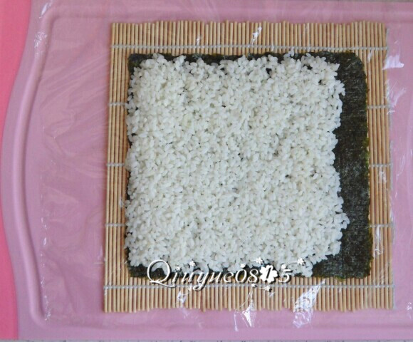 基础寿司,寿司帘上铺一张保鲜膜，放紫菜，把米饭铺匀。紫菜其中一端留出一点空边（此图片是为说明保鲜膜等用法）。