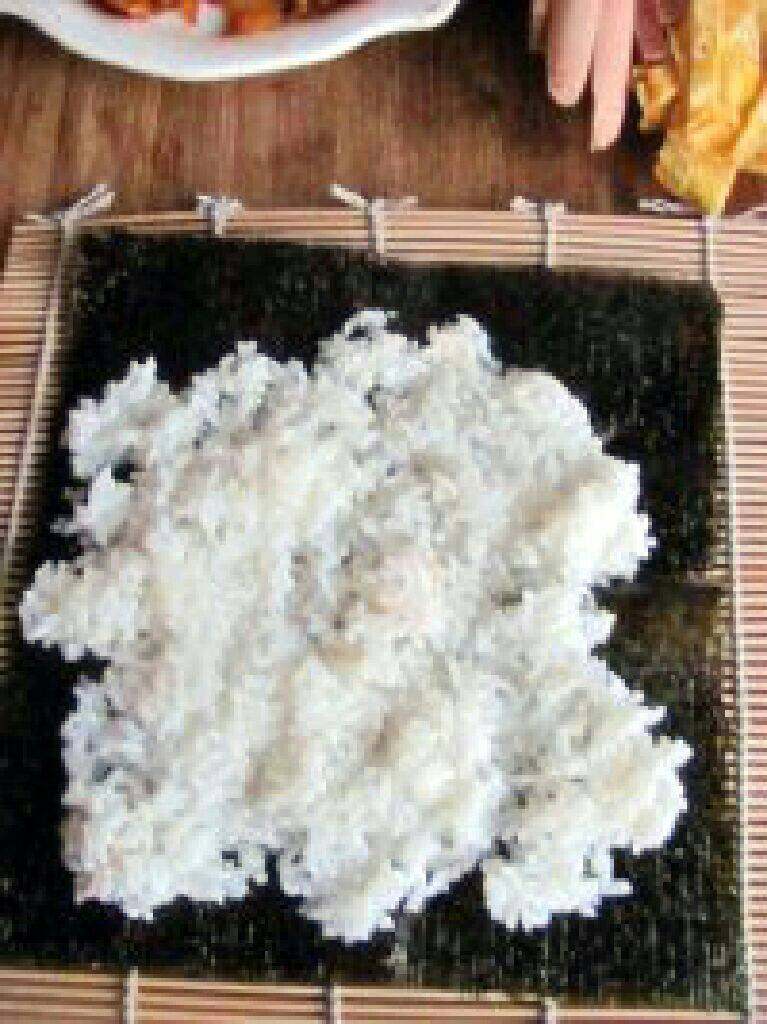 紫菜泡菜包饭,寿司卷帘上放海苔，然后把米饭均匀的铺在紫菜上。
