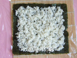 翻转樱花寿司,寿司帘上铺一张保鲜膜，放海苔，把米饭铺匀。海苔其中一端留出一点空边