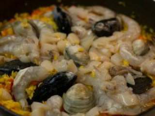 西班牙海鲜饭,汤汁看着收尽的时候，码放好海鲜，用锅铲轻压几下，挤入柠檬汁。加盖5分钟。