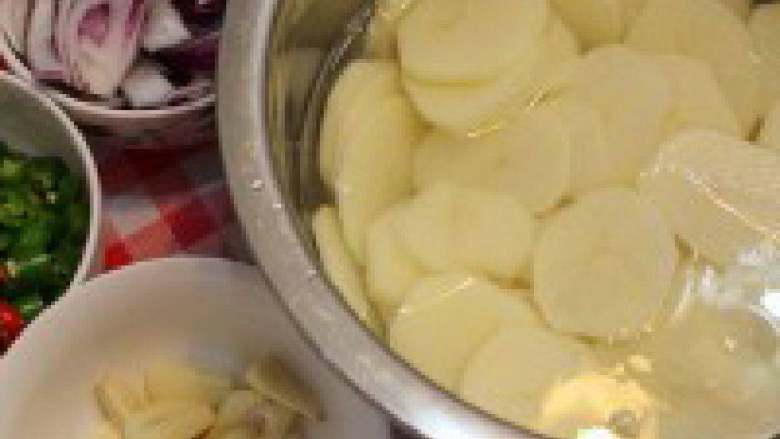 干锅土豆,土豆切片后过水清除表面的淀粉、洋葱切块、青红辣椒切段、蒜切片。