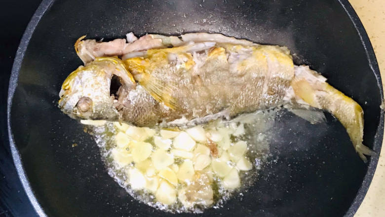 茄汁黄鱼,把黄鱼推到锅的一边，加入大蒜片，煸炒出蒜香
