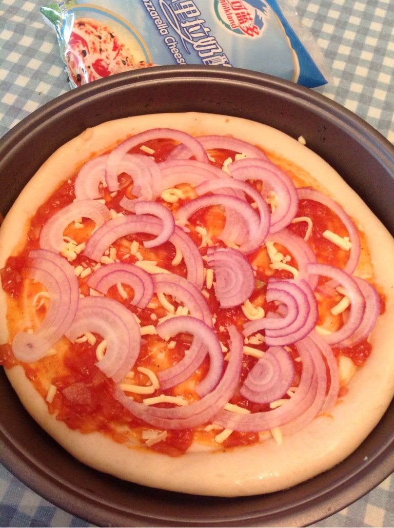 培根披萨,如图披萨饼皮常温解冻后，底部周边刷上色拉油，表面均匀刷上披萨酱，撒上少许奶酪丝，铺上洋葱丝