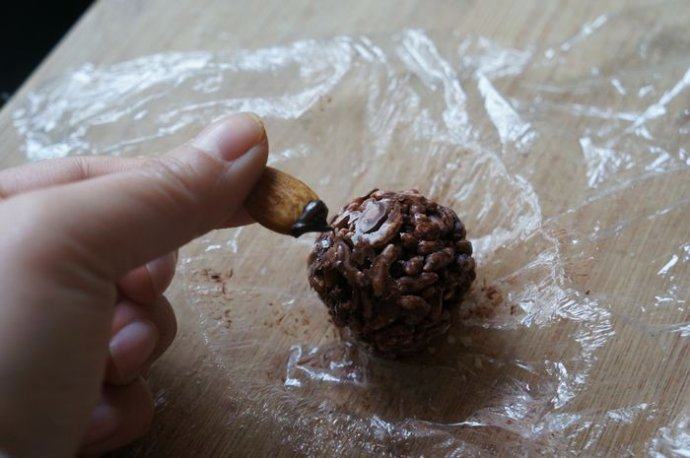 巧克力杏仁脆香米,凝固好的巧克力杏仁脆香米球，小心的揭去外面的保鲜膜。取完整大杏仁，底部沾点融化的巧克力，沾在球上即可
