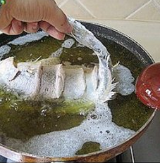 糖醋黄鱼,慢慢的把鱼身子放进油锅里，一只手提着鱼尾巴，另一只手拿着勺子要将鱼头抬起