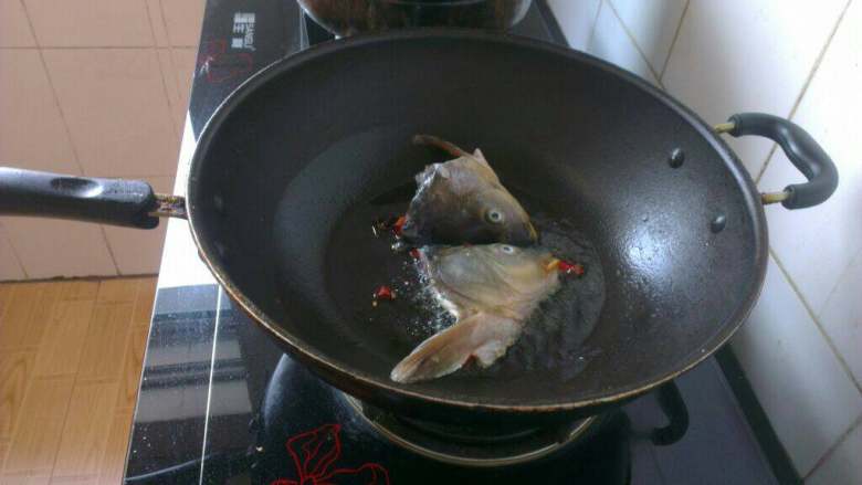 鱼头炖豆腐,炒锅倒油烧热，放入两半鱼头煎至两面变色；