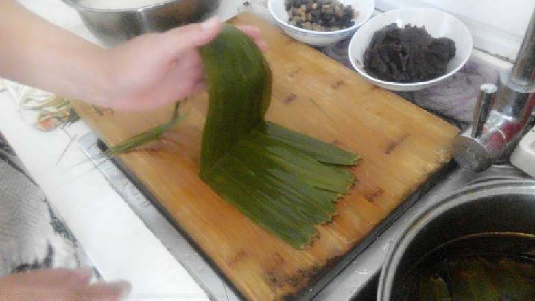 豆沙蜜豆粽子,把八片粽叶平铺在菜板上不能有缝隙，用手淋点水在粽叶上，然后折一下如有图